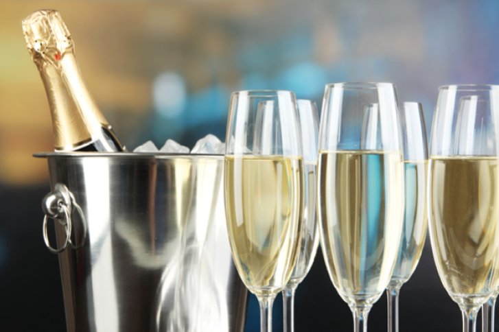 Ein Champagnerkühler mit Flasche steht neben vier gefüllten Gläsern in festlicher Umgebung.