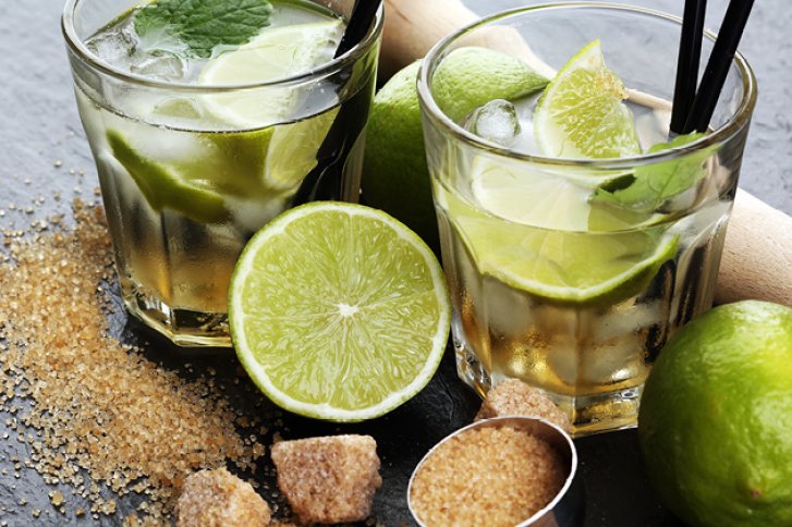 Zwei Gläser mit Limettenscheiben und Eis sind umgeben von Zucker und ganzen Limetten.