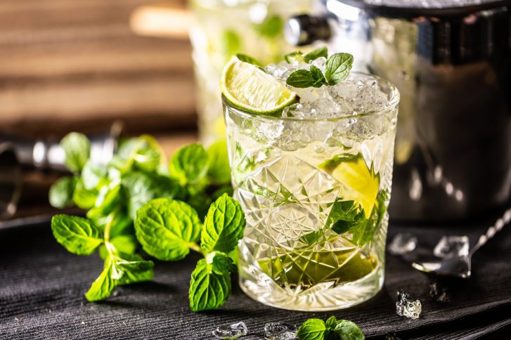 Ein Glas Mojito mit Eis, Limette, und Minze auf einem dunklen Untergrund.