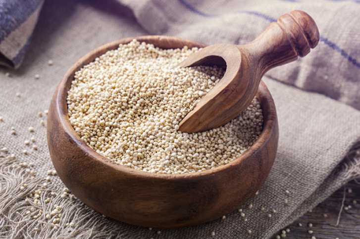 Eine Holzschale mit Quinoa und einem Löffel steht auf einem Leinentuch.