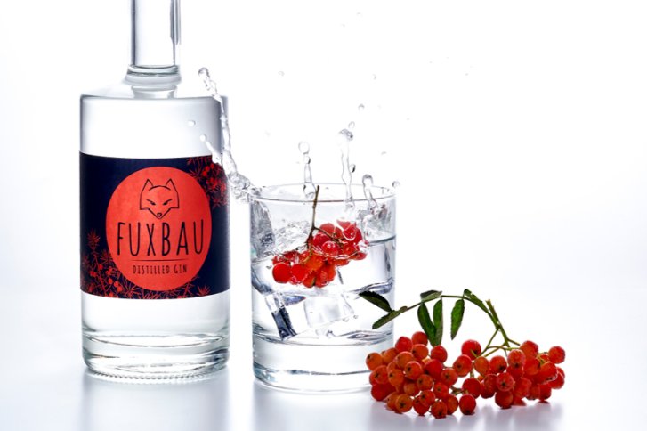 Flasche Gin steht neben Glas mit Eis und Beeren, spritzendes Wasser auf weißem Hintergrund.