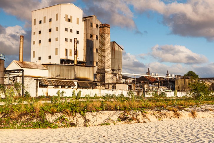 Eine alte Fabrik steht still in einer ländlichen Landschaft bei Sonnenschein und Wolken.