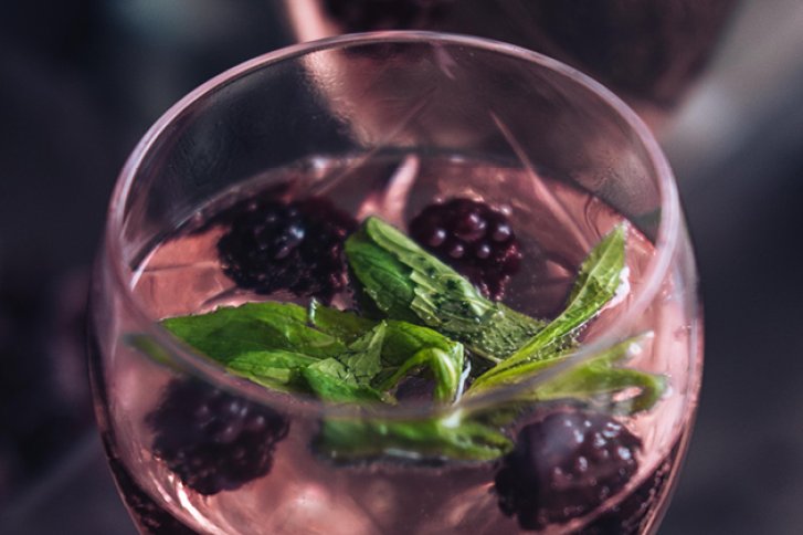 Ein Weinglas enthält Brombeeren und Minzblätter, umgeben von einem dunklen, unscharfen Hintergrund.