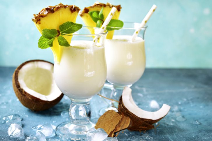 Zwei Pina Colada Cocktails mit Ananasscheiben und Minze, umgeben von Kokosnusshälften auf Eis.
