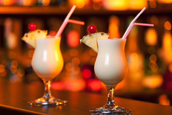 Zwei Cocktails mit Kirschen und Ananas, auf Bar in warm beleuchteter Umgebung.