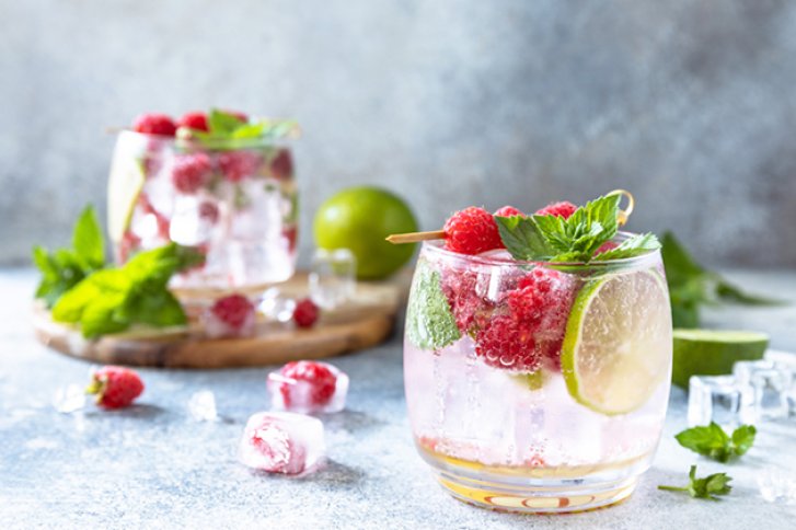 Getränk steht mit Himbeeren, Minze und Limetten dekoriert, auf einem grauen Tisch.