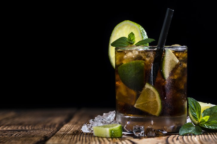 Cocktail mit Limetten und Minze, steht mit Eiswürfeln auf einem rustikalen Holztisch.