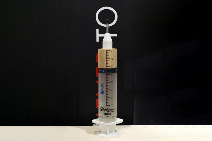 Große Spritze steht auf einer hellen Fläche, beschriftet mit "Delicana Wodka" und Skala.