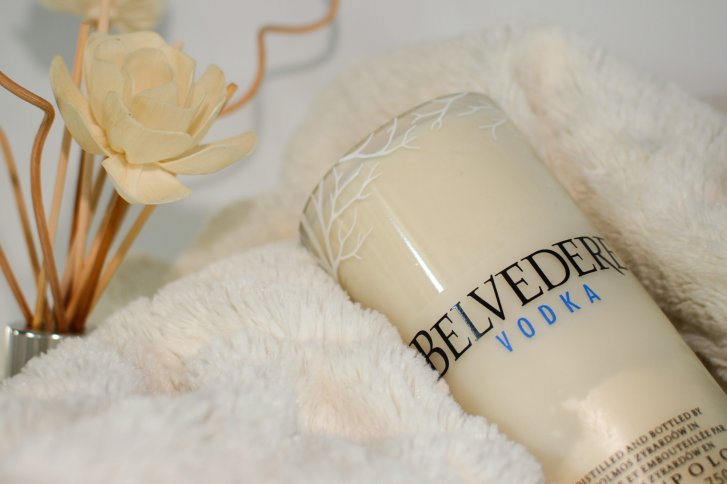 Flasche Belvedere Vodka liegt auf weichem, cremefarbenem Stoff neben einer dekorativen Blume.