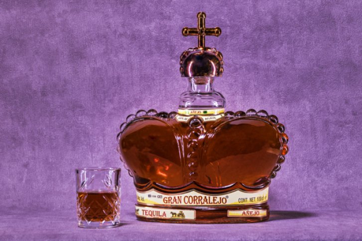 Ein kronenförmiger Gran Corralejo Tequila Añejo auf lila Hintergrund mit Glas daneben.