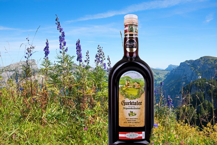 Flasche "Gurktaler Alpenkräuter" steht in einer alpinen Wiesenlandschaft mit Bergen im Hintergrund.