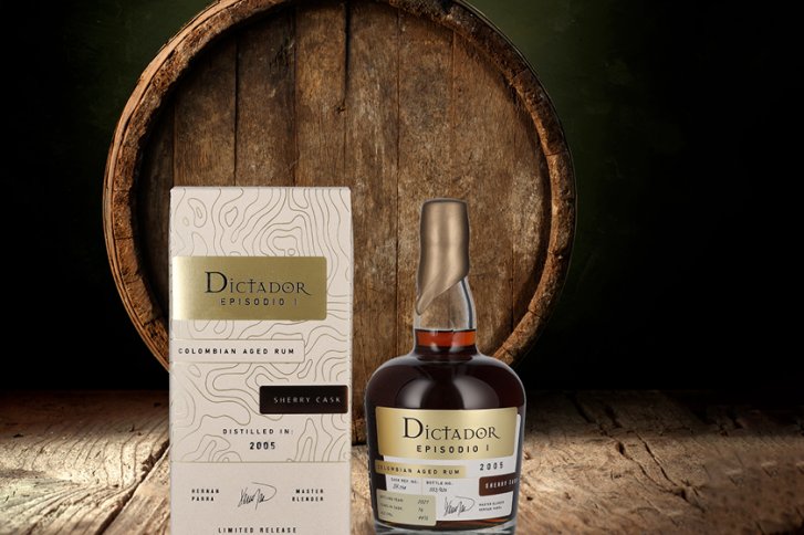 Flasche und Verpackung Rum "Dictador" stehen vor einem rustikalen Holzfass auf Holztisch.