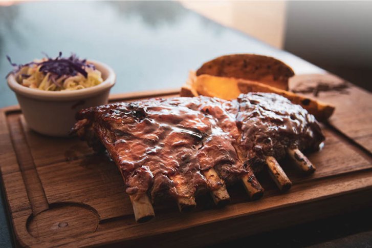 Rippchen liegen auf Holzteller, begleitet von Krautsalat und Brot in einem Restaurantambiente.