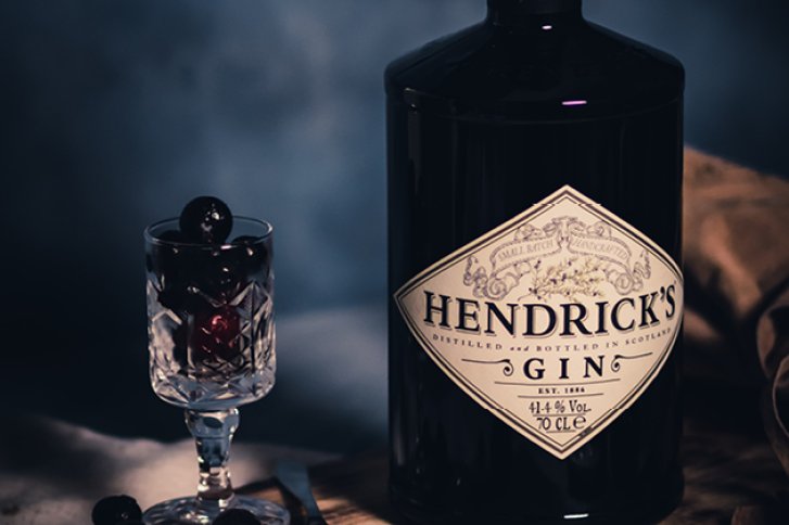 Eine Hendrick's Gin-Flasche steht neben einem Glas mit Kirschen auf einem Holztisch.