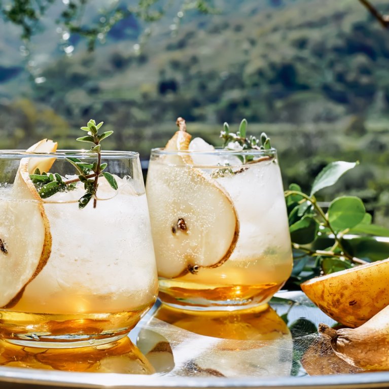 Two glasses of pear drinks and herbs are placed on a tray outside.