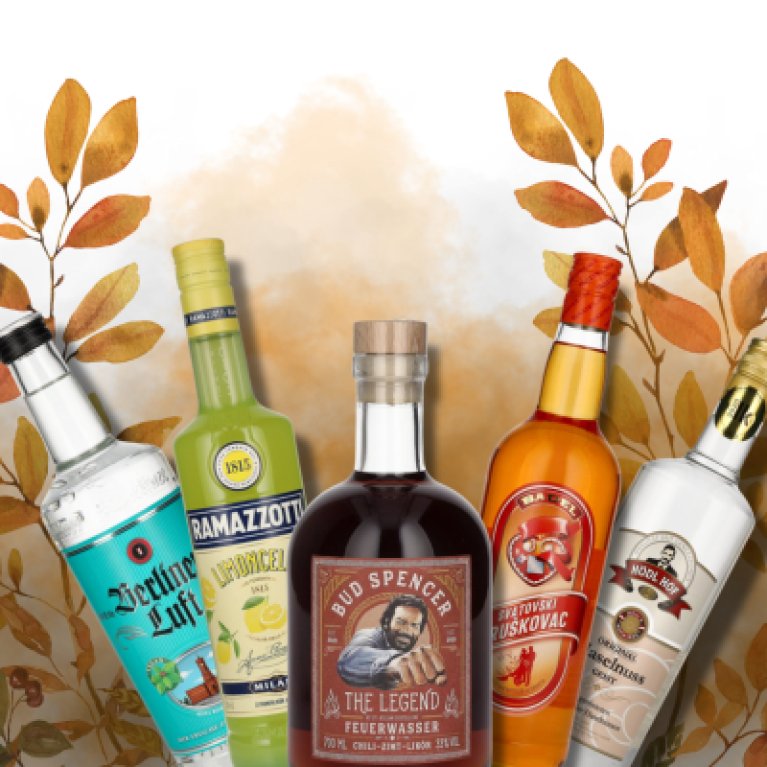 Vijf kleurrijke flessen sterke drank staan voor een herfstachtige achtergrond met bladeren.