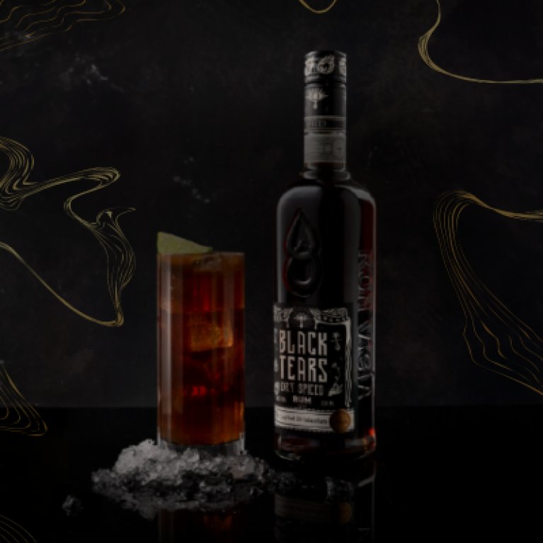 Une photo de produit prise de face montre une bouteille de rhum Black Tears avec, à côté, un verre contenant du rhum, des glaçons et du citron sur un fond sombre.