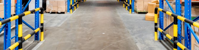 Des cartons sont stockés sur des étagères bleues, le long d'un long couloir dans un grand entrepôt.