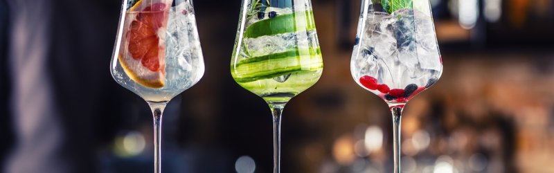 Three wine glasses with decorated cocktails stand on a wooden counter in a bar setting.