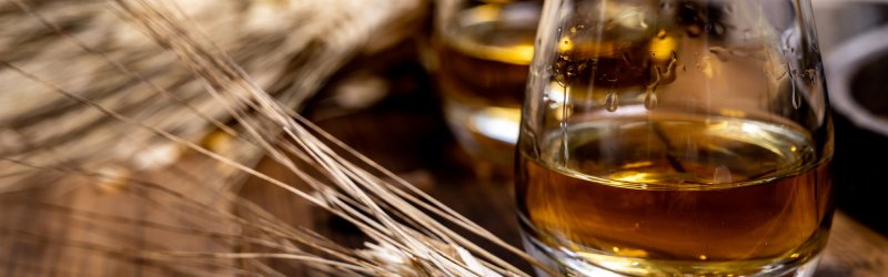 Een glas whisky staat op een houten tafel naast korenaren.