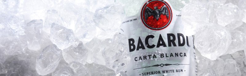 Bacardi-Flasche liegt gekühlt im Eis, umgeben von vielen durchsichtigen Eiswürfeln.