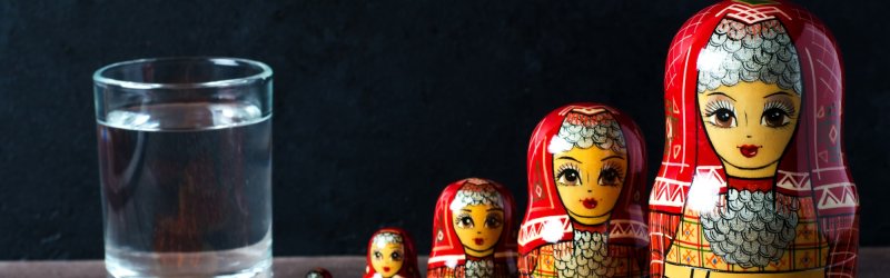 Glass of water, bread with caviar and matryoshka dolls on a wooden table against a dark background.