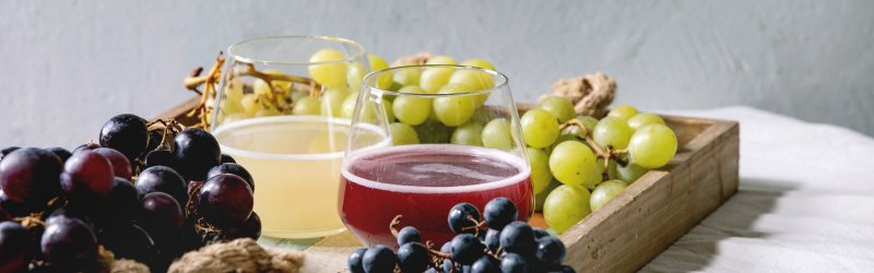 Gläser mit rotem und gelbem Saft stehen auf Holztablett, umgeben von frischen Trauben.