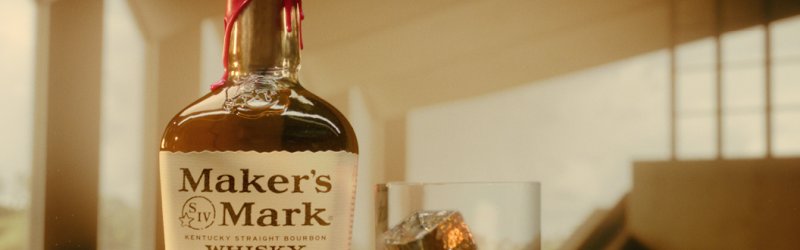 Une bouteille de whisky Maker's Mark est posée sur la table à côté d'un verre de whisky et de glaçons.