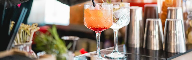 Gläser – stehen – auf einer Bar mit verschiedenen Cocktails und metallischen Shakern im Hintergrund.