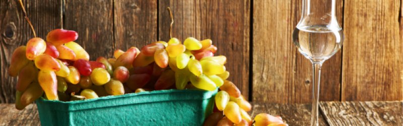 Grappa mit Trauben in türkisen Becher auf Hintergrund aus Holz