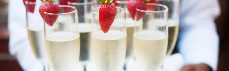 Champagne glasses with strawberries are served on a tray by one person.