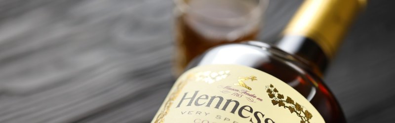 Bottle of Hennessy Cognac on the table, glass in the background, black and gray wooden background.