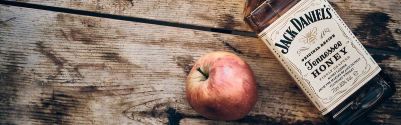 Whiskeyflasche liegt neben einem frischen Apfel auf einem alten Holztisch.