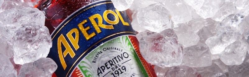 Bottle of Aperol lies in ice cubes, the colorful label with the lettering is visible.