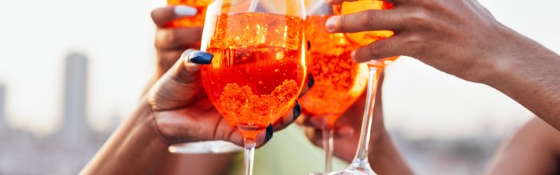 Glazen met oranje drank proosten, buiten met een wazige skyline op de achtergrond.