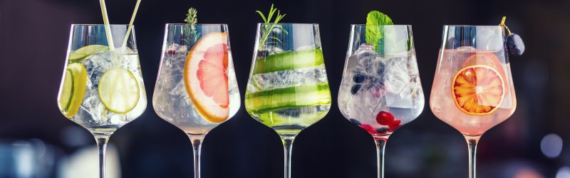 Fünf Weingläser, gefüllt mit bunten Cocktails und frischen Früchten, auf einem Holztisch platziert.