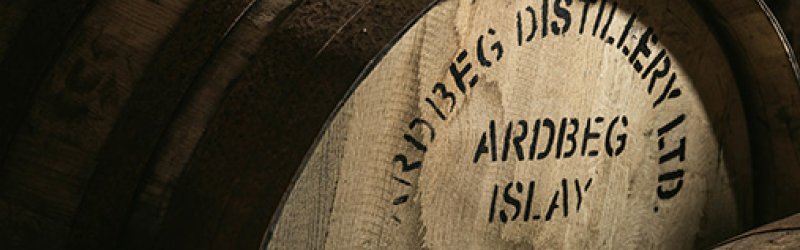 Le fût en bois portant l'inscription "Ardbeg Distillery Ltd" se trouve dans un environnement de stockage sombre.