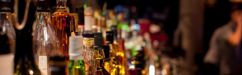 Verschiedene Flaschen stehen dicht nebeneinander auf einer Bar in einer dunklen Umgebung.