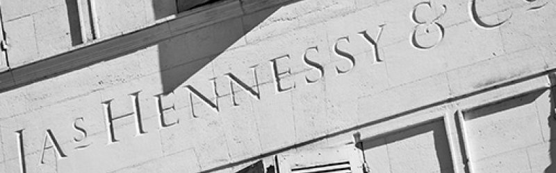 Op het gebouw staan "Jas Hennessy & Co" letters met gesloten luiken, in het zonlicht.
