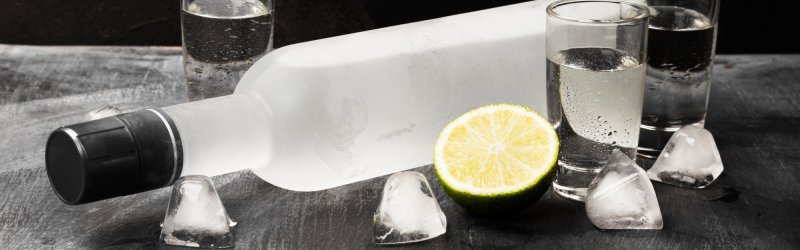 Bevroren wodkafles ligt tussen twee glazen en ijsblokjes op een zwart oppervlak.