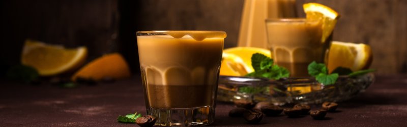 Ein Glas mit cremigem Getränk steht auf einem Tisch, umgeben von Orangen und Minze.