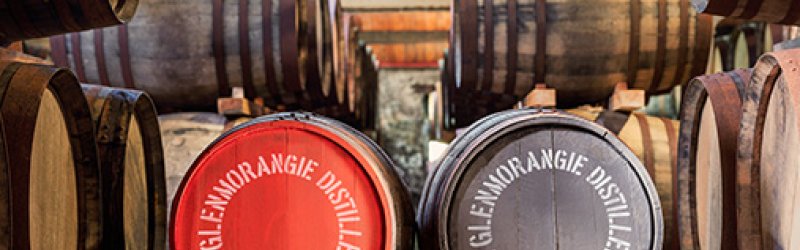 Houten vaten liggen in een magazijn. Twee vaten met "THE GLENMORANGIE DISTILLERY" goed zichtbaar.
