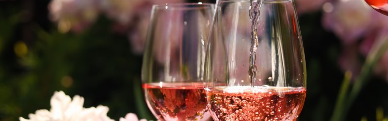 Deux verres à vin sont remplis de vin rosé, dans un jardin en fleurs.