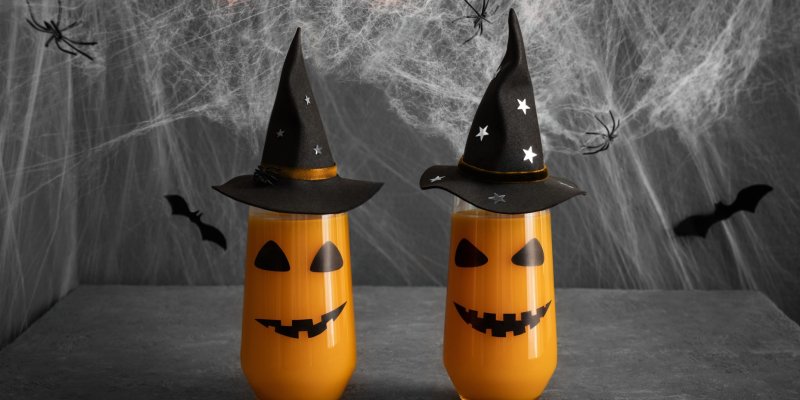 Zwei Halloween-Gläser mit Zauberhüten, gruselige Gesichter, vor Spinnweben und schwarzen Fledermäusen.