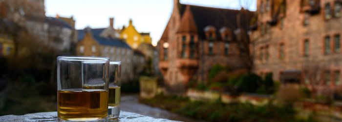 Twee glazen whisky staan stil op een borstwering, met een vage, historische stad op de achtergrond.