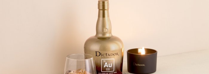 Une bouteille de rhum et un verre sont posés à côté d'une bougie allumée sur une surface claire.