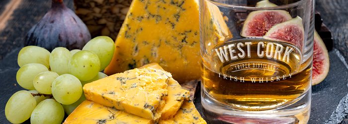 Une prise de vue en plongée montre une planche de bois rustique avec du fromage, des raisins, des figues et un verre de liquide ambré sur un fond flou. La scène est bien éclairée, ce qui permet de mettre en valeur les textures et les couleurs des e