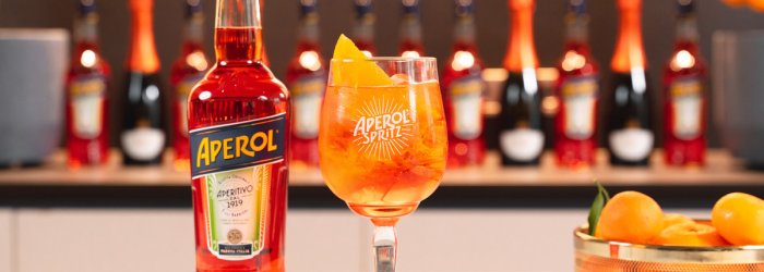 Aperolfles en Aperol spritsglas op tafel, sinaasappels en flessen op de achtergrond.