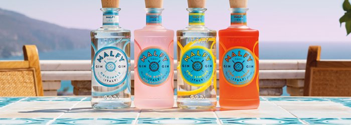 Vier kleurrijke flessen jenever staan op een decoratieve tafel met uitzicht op zee in een zonnige omgeving.