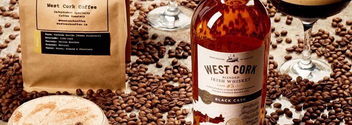 An eye-level close-up shows a variety of objects associated with West Cork Distillers against a background of scattered coffee beans in a warm hue.